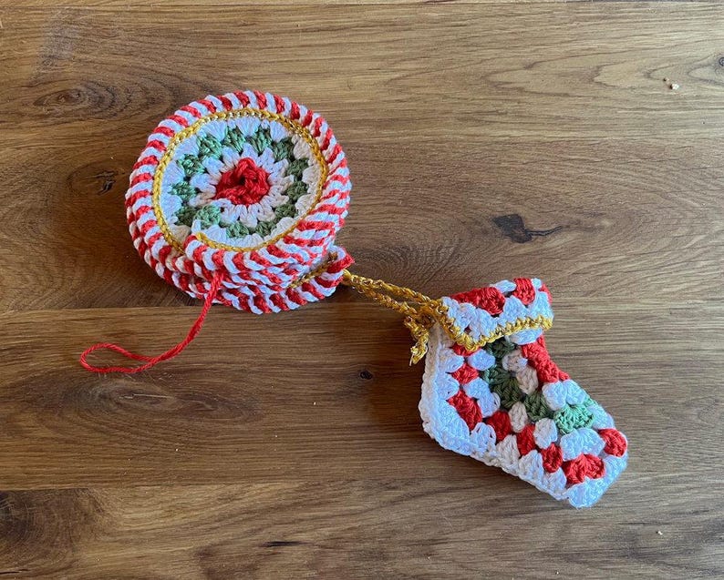May include: Crocheted Christmas ornament set featuring a round coaster and a small stocking. The coaster has a red, white, and green design with a red center. The stocking is white with red and green accents, and a gold trim.