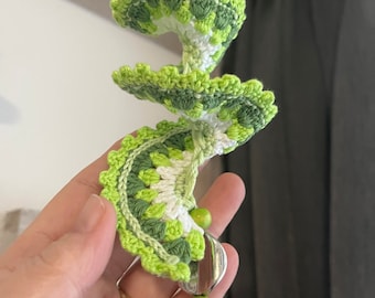 May include: A green and white crocheted spiral with a green and white beaded tassel. The spiral is made of multiple layers of crocheted fabric.