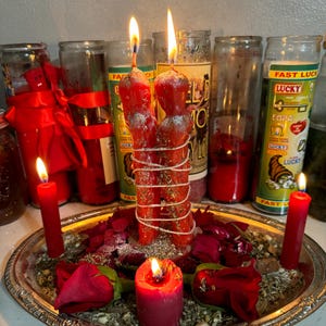 May include: A silver tray with red candles, rose petals, and dried herbs. Two red candles are tied together and are lit. The candles are surrounded by smaller red candles.