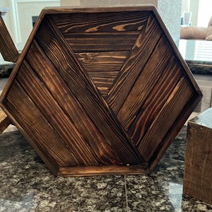Op de afbeelding: Drie houten woonaccessoires: een zeshoekige dienblad met een donkere houtkleur, een stervormige wanddecoratie en een vierkante tissueboxhoes. Alle items zijn gemaakt van donker hout met een rustieke afwerking.