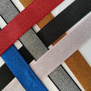Könnte beinhalten: Sortiment an glitzerndem elastischem Besatz in verschiedenen Farben, darunter Rot, Blau, Silber, Gold und Pink. Der Besatz ist etwa 2,5 cm breit und hat eine glitzernde Oberfläche.