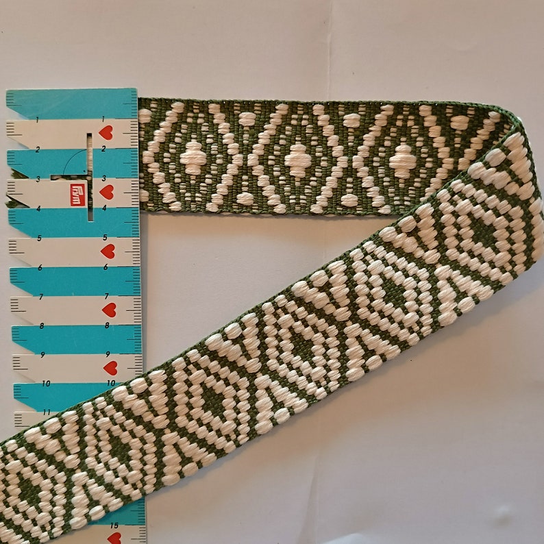 Puede incluir: Cinta tejida con un patr&oacute;n de diamantes repetido en blanco y verde oliva. La cinta se mide con una regla azul y blanca. La cinta mide aproximadamente 3,8 cm de ancho.