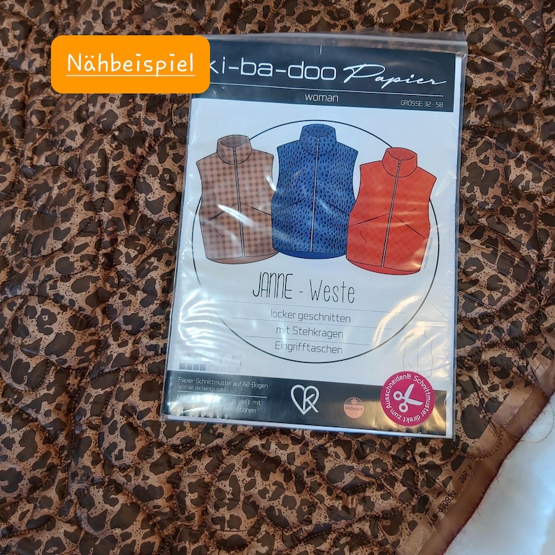 May include: A sewing pattern package with the text "N&auml;hbeispiel" in an orange box. The package features illustrations of three vests in brown, blue, and orange. The text "JANNE-Weste" is visible.