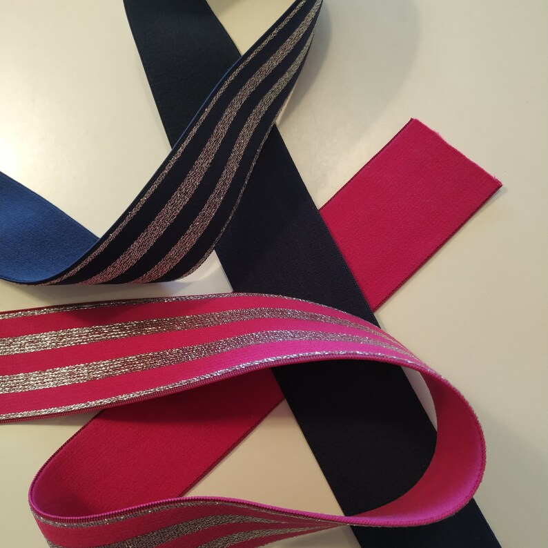 K&ouml;nnte beinhalten: Nahaufnahme von farbigen B&auml;ndern in Marineblau, Pink und Fuchsia. Ein Band hat silberne Metallic-Streifen. Die B&auml;nder sind in einem flie&szlig;enden, sich &uuml;berlappenden Muster angeordnet, das eine interessante Textur und Farbkombination erzeugt.