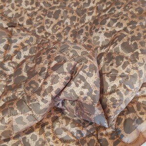 May include: A quilted blanket with a leopard print pattern in shades of brown and tan. The blanket has a diamond-shaped stitching pattern and a soft, textured appearance. The fabric appears to be lightweight and suitable for layering.