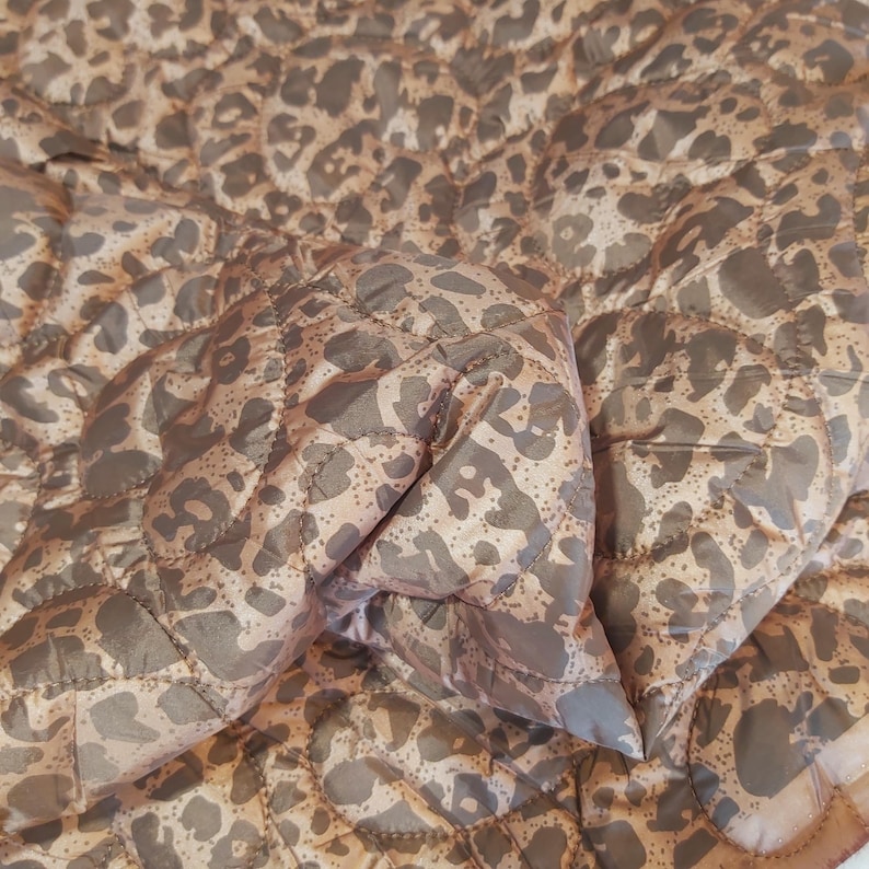 May include: A quilted blanket with a leopard print pattern in shades of brown and tan. The blanket has a diamond-shaped stitching pattern and a soft, textured appearance. The fabric appears to be lightweight and suitable for layering.