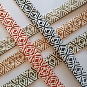 Puede incluir: Primer plano de varias correas de tela tejida en varios colores, incluyendo rojo, azul marino, verde oliva y beige. Cada correa presenta un patr&oacute;n de diamantes repetido en blanco, creando un dise&ntilde;o texturizado. Las correas est&aacute;n dispuestas en un patr&oacute;n entrecruzado.