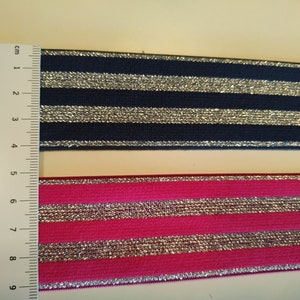 K&ouml;nnte beinhalten: Zwei Streifen gestreiftes elastisches Band. Einer ist marineblau mit silbernen Streifen, der andere pink mit silbernen Streifen. Ein Lineal liegt neben den B&auml;ndern, mit Messungen in Zentimetern.