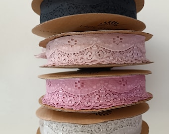 May include: Four spools of lace trim, stacked on top of each other. The spools are wrapped in brown paper and have a label that says "Lace Trim". The lace trim is in four different colors: black, pink, light pink, and white.