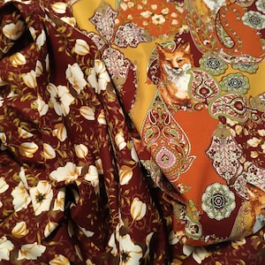 Könnte beinhalten: Zwei Stoffmuster mit unterschiedlichen Mustern. Eines ist ein burgunderfarbener Stoff mit weißen Blumenmustern. Das andere ist ein rostfarbener Stoff mit einem Paisley-Muster und einem Fuchs-Motiv.