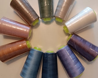 Könnte beinhalten: Sortiment von 12 Garnrollen in verschiedenen Farben, darunter rosa, braun, blau, grün und weiß. Die Rollen sind in einem Kreis auf einer weißen Oberfläche angeordnet.