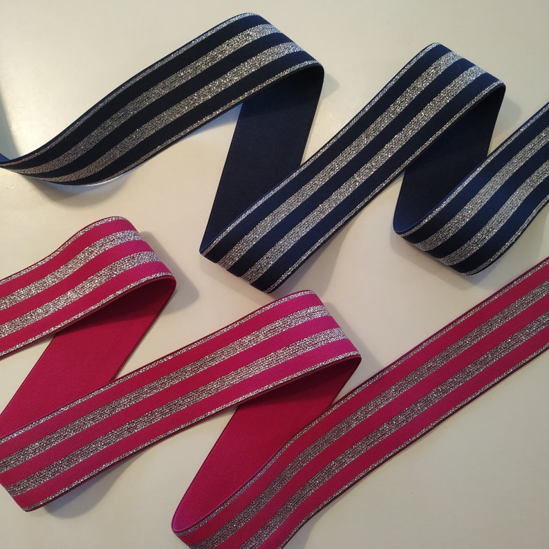 K&ouml;nnte beinhalten: Zwei B&auml;nder, eines in Marineblau und eines in Fuchsia, werden gezeigt. Beide B&auml;nder haben horizontale silberne Glitzerstreifen. Die B&auml;nder sind in einem wellenf&ouml;rmigen Muster angeordnet, das ihre Textur und ihr Design hervorhebt.
