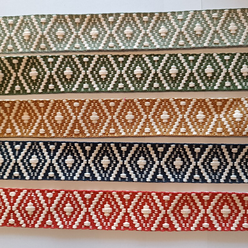 Puede incluir: Primer plano de seis cintas tejidas con un patr&oacute;n de diamantes repetido. Las cintas son de varios colores: verde claro, verde oscuro, dorado, azul marino y rojo. El patr&oacute;n de diamantes es blanco.