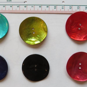 Könnte beinhalten: Sechs runde, flache, irisierende Knöpfe mit jeweils zwei Löchern. Die Knöpfe sind in den Farben Türkis, Grün, Rot, Schwarz und zwei Rottönen.