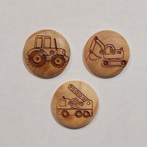 Könnte beinhalten: Drei Holz-Knöpfe mit verschiedenen Fahrzeugdesigns. Die Knöpfe sind rund und haben zwei Löcher. Die Designs sind ein Traktor, ein Bagger und ein Feuerwehrauto.