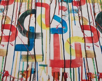 May include: White fabric with a colorful abstract design. The pattern features large, stylized letter-like shapes in red, blue, and green, with black drips and vertical stripes in various colors. The fabric is rolled up.