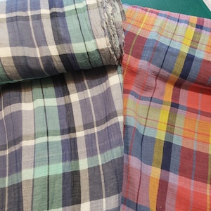 Könnte beinhalten: Zwei Stoffstücke mit karierten Mustern. Ein Stoff ist blau, grün und weiß. Der andere Stoff ist rot, orange, gelb und blau.