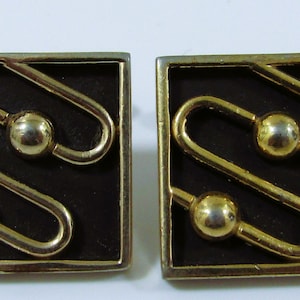 May include: A pair of gold cufflinks with a black enamel background. The cufflinks feature a geometric design with three gold circles.