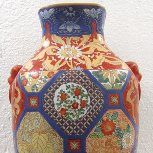 May include: A large, decorative, ceramic vase with a blue, red, and gold geometric pattern. The vase has a wide, round body and a narrow neck. The vase is decorated with floral and leaf motifs.