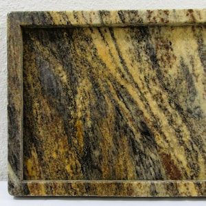 May include: Rectangular serving tray with a raised border. The tray features a natural stone pattern with swirling veins of brown, black, and yellow. The tray is made of a solid, heavy material.