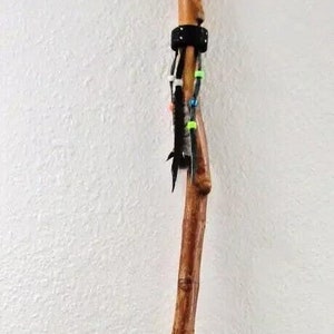 May include: A wooden walking stick with a carved animal head at the top. The stick is decorated with black leather, feathers, and colorful beads.