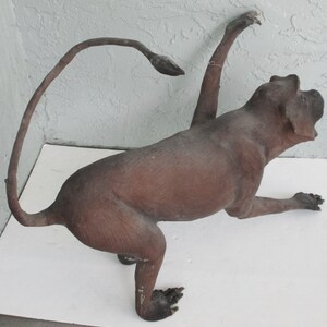 May include: A brown, taxidermied monkey figurine with a long tail curled behind it. The monkey is posed in a sitting position with its right arm raised and its left arm extended forward.