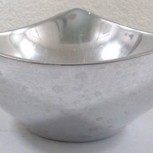 Puede incluir: Un cuenco de metal plateado con un dise&ntilde;o curvo &uacute;nico. El cuenco tiene una superficie lisa y reflectante con motas sutiles.