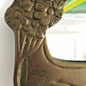 May include: A vintage brass mirror with a floral design. The mirror is rectangular and has a beveled edge. The frame is decorated with a cluster of flowers and leaves.