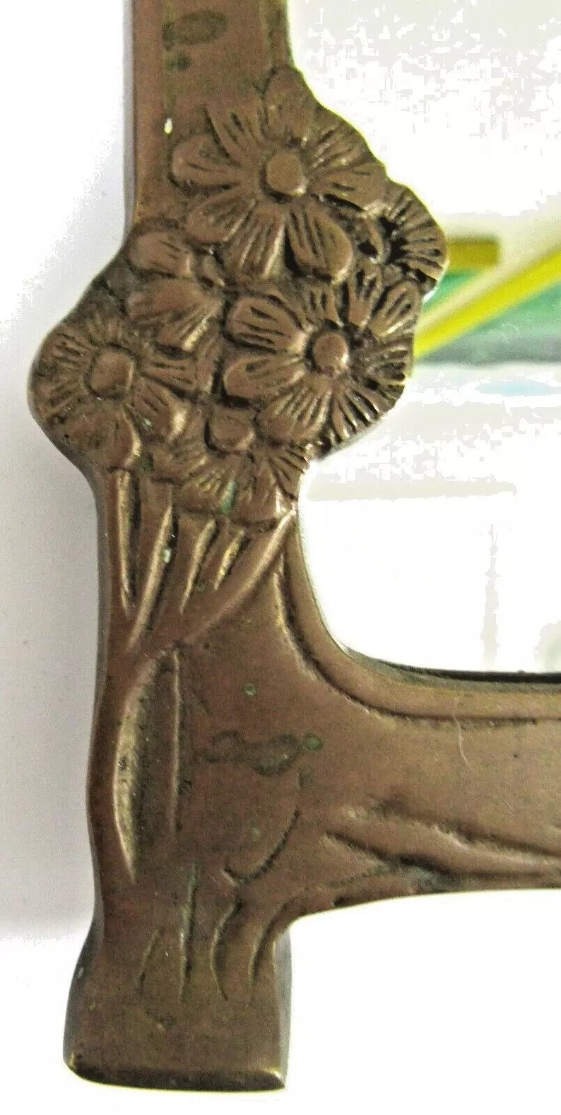 May include: A vintage brass mirror with a floral design. The mirror is rectangular and has a beveled edge. The frame is decorated with a cluster of flowers and leaves.