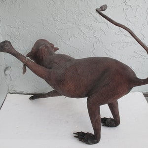 May include: A brown leather monkey sculpture with a long tail. The monkey is posed in a sitting position with its arms outstretched.