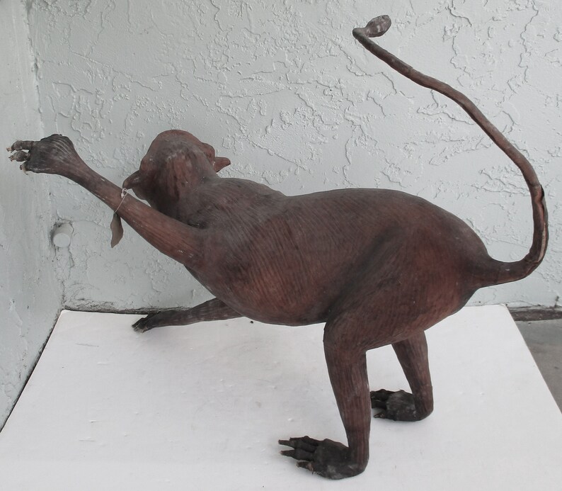 May include: A brown leather monkey sculpture with a long tail. The monkey is posed in a sitting position with its arms outstretched.