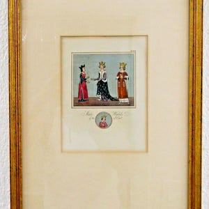 May include: Framed print featuring a historical illustration of three figures in ornate attire, possibly royalty. The figures are depicted in a colorful, detailed style, with text at the bottom. The frame is gold-colored.