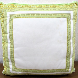 May include: A white pillow with a green and gold border. The border features a repeating geometric pattern.