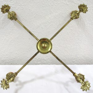 May include: A gold metal stand with four decorative arms and a round center piece. The stand is designed to hold four items, such as candles or vases.