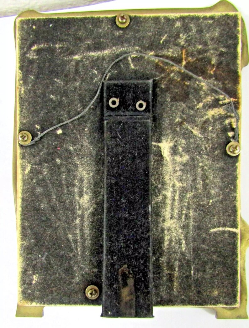 May include: The back of a brass picture frame with a black felt backing and a black hanging wire. The frame has four small brass feet.