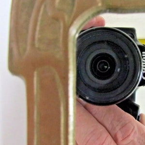 May include: A close-up of a black camera lens with a silver ring around the lens. The camera is being held by a hand.
