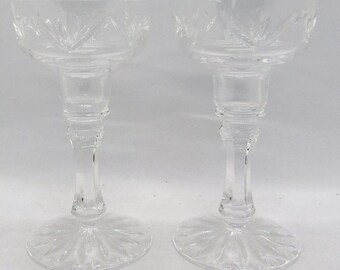 May include: Two clear glass candle holders with a cut glass design. The holders have a wide base and a tall, slender stem.