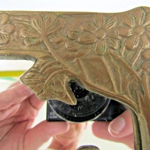 May include: A brass mirror frame with an ornate floral design. The frame is a light gold color and has a raised design of flowers and leaves.