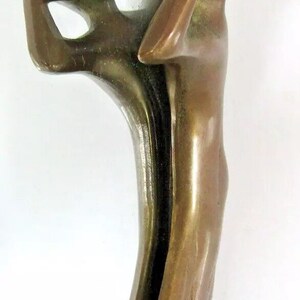 May include: A bronze mirror with a decorative frame featuring two stylized figures. The figures are sculpted in a flowing, organic style, with their bodies intertwined. The mirror is oval-shaped and has a beveled edge.