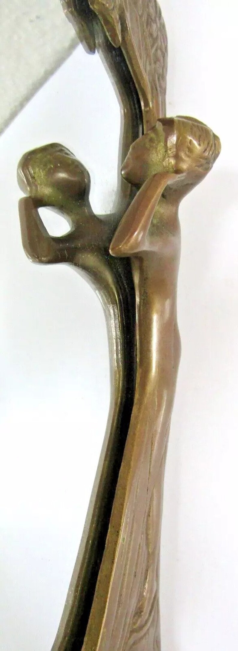 May include: A bronze mirror with a decorative frame featuring two stylized figures. The figures are sculpted in a flowing, organic style, with their bodies intertwined. The mirror is oval-shaped and has a beveled edge.