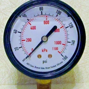 Puede incluir: Un manómetro blanco con una aguja negra y un bisel negro. El manómetro lee hasta 160 psi y 1100 kPa. El manómetro tiene el texto "ABS Case, Bronze Tube, Brass Socket, Silicone" impreso en la cara.