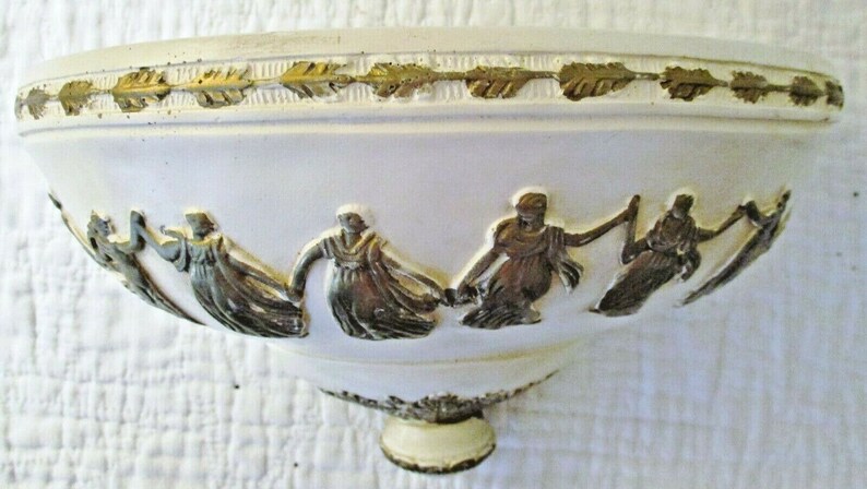 May include: White ceramic bowl with a gold trim and a raised design of figures in flowing robes. The bowl has a rounded base.