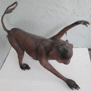 May include: A brown wooden monkey sculpture with blue eyes. The monkey is standing on all fours with its arms outstretched.