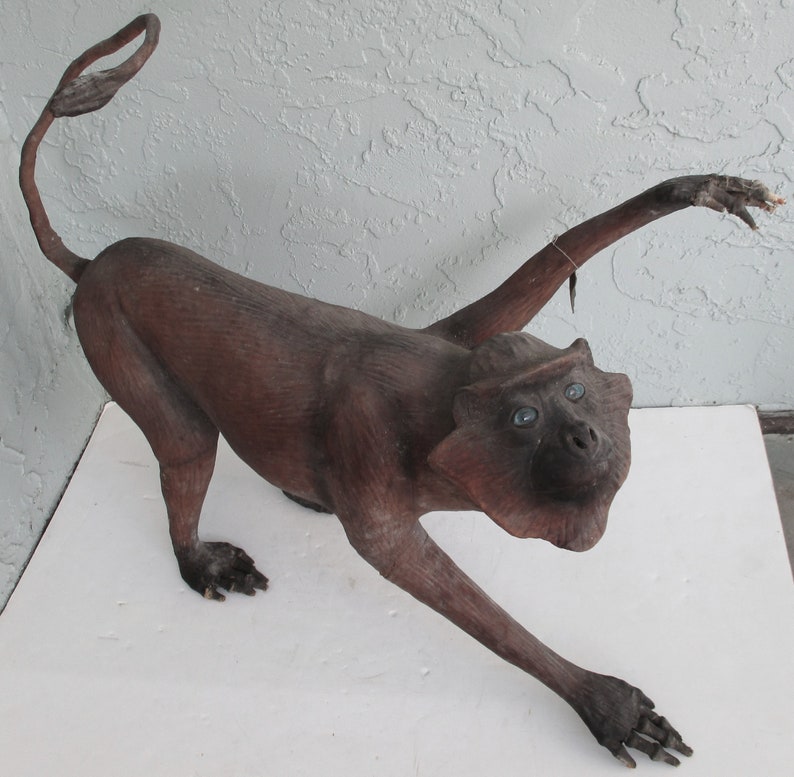 May include: A brown wooden monkey sculpture with blue eyes. The monkey is standing on all fours with its arms outstretched.