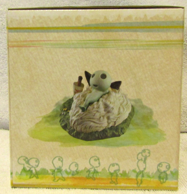 May include: A small, gray, figurine of a creature with large eyes and a long, thin body, sitting on a white, fluffy cloud. The figurine is surrounded by a green, grassy area. The background is a light brown with a pattern of yellow and green stripes.