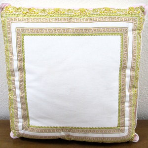May include: A white pillow with a pink and gold Greek key pattern border.