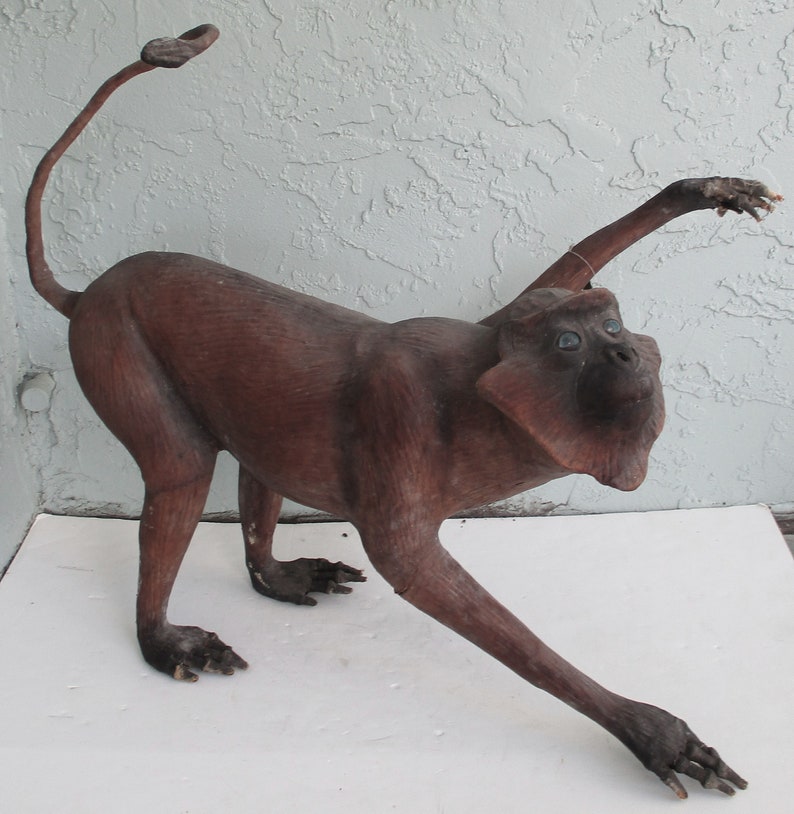 May include: A brown wooden monkey sculpture with a long tail and outstretched arms. The monkey has blue eyes and a realistic appearance.