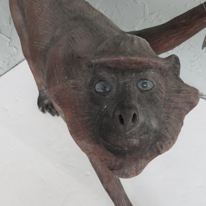 May include: A wooden monkey sculpture with blue eyes. The monkey is standing on all fours and has a long tail.