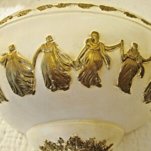 May include: White ceramic bowl with a gold trim and embossed design of figures in a circle. The figures are wearing long robes and appear to be dancing.