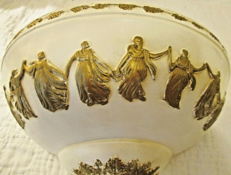 May include: White ceramic bowl with a gold trim and embossed design of figures in a circle. The figures are wearing long robes and appear to be dancing.